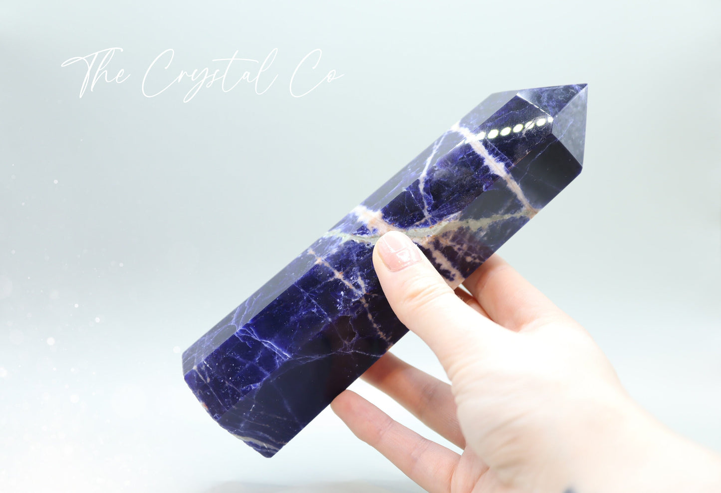 Sodalite crystal tower with deep blue hues and natural white veins. Polished to a smooth finish, standing upright with a pointed top. Perfect for home decor, meditation, or crystal collections. Unique and eye-catching, showcasing its natural beauty.