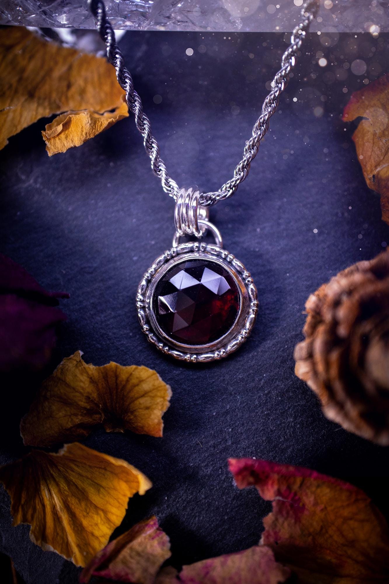 Handmade sterling silver pendant necklace featuring a circular design with a deep red garnet crystal centrepiece, showcasing a minimalist yet elegant artisan style. This piece has been created using recycled fine and sterling silver and features a gorgeous rose cut garnet that is full of sparkle. Suitable or special occasions such as birthdays, anniversaries, graduations and more. Garnet is the birthstone for January. Witchy and gothic handmade jewellery.