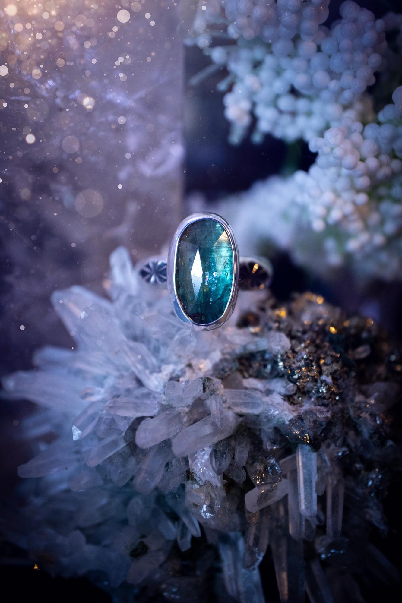 Beautiful and handcrafted, natural teal green kyanite crystal, staking ring. This stunning ring has been hand made using fine and sterling silver. It features a beautiful and natural teal green kyanite crystal that has rainbows and flash, such a gorgeous colour. The ring shank on this ring has been stamped with a gothic pattern to give it a one of a kind vibe. Ideal gift for that special person in your life, or for any crystal and jewellery lover. Hippy, witchy and gothic jewellery for the soul.