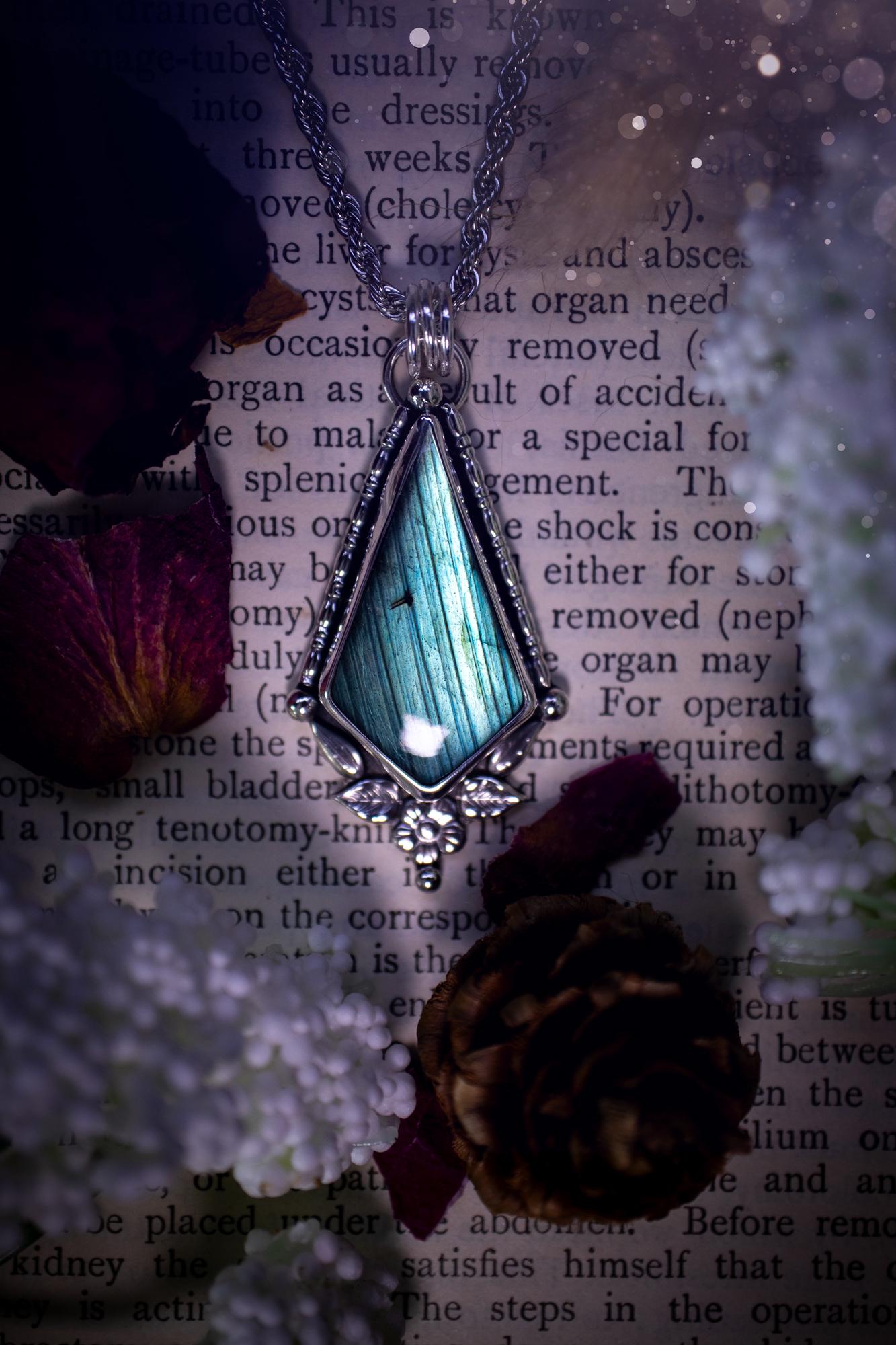 This stunning pendant necklace has been handcrafted using a mix of recycled fine and sterling silver. Featuring a beautiful and natural green and blue hued labradorite crystal that is full of flash! accompanying this magical crystal is a mix of fae inspired components such as little leaves, flower, silver balls and gothic gallery wire. A true bespoke piece with no other being the same! Ideal for any crystal and jewellery lover that loves a witchy and gothic vibe, along with the beauty of nature!