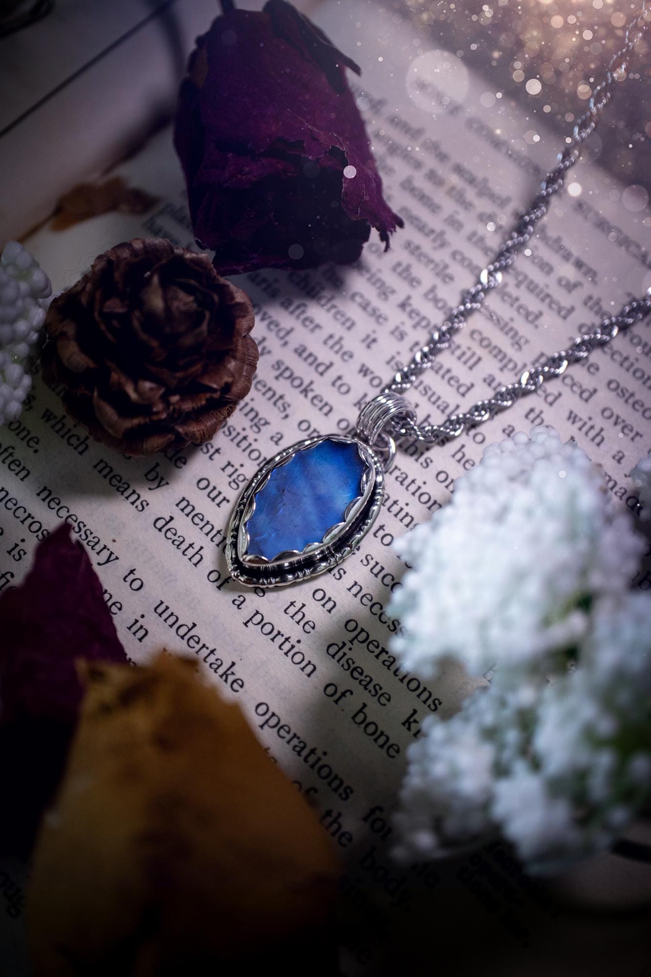A handmade rainbow moonstone pendant necklace featuring a glowing, iridescent moonstone with blue and purple flashes. The stone is set in a scallop bezel, framed by bespoke gothic gallery wire that adds both hippy and witchy vibes. Crafted from sterling and fine silver, the pendant hangs on a silver chain, exuding mystical charm and alternative style. A one-of-a-kind piece with gothic, and magical energy. The ideal gift for crystal and jewellery lovers. Moonstone is the birthstone for June.