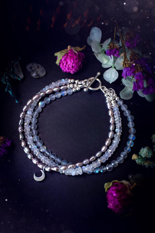 Stunning and handcrafted, triple crystal beaded bracelet. This beautiful bracelet consists of three bracelets in one all held together with a sterling silver t-bar toggle clasp. Featuring stunning flashy rainbow moonstone, light coloured labradorite, and grey to purple fresh water pearls. The findings on this bracelet are sterling silver, with a stainless steel moon charm. This piece is totally bespoke and full of celestial vibes. Ideal for any crystal and jewellery lover. Witchy and gothic