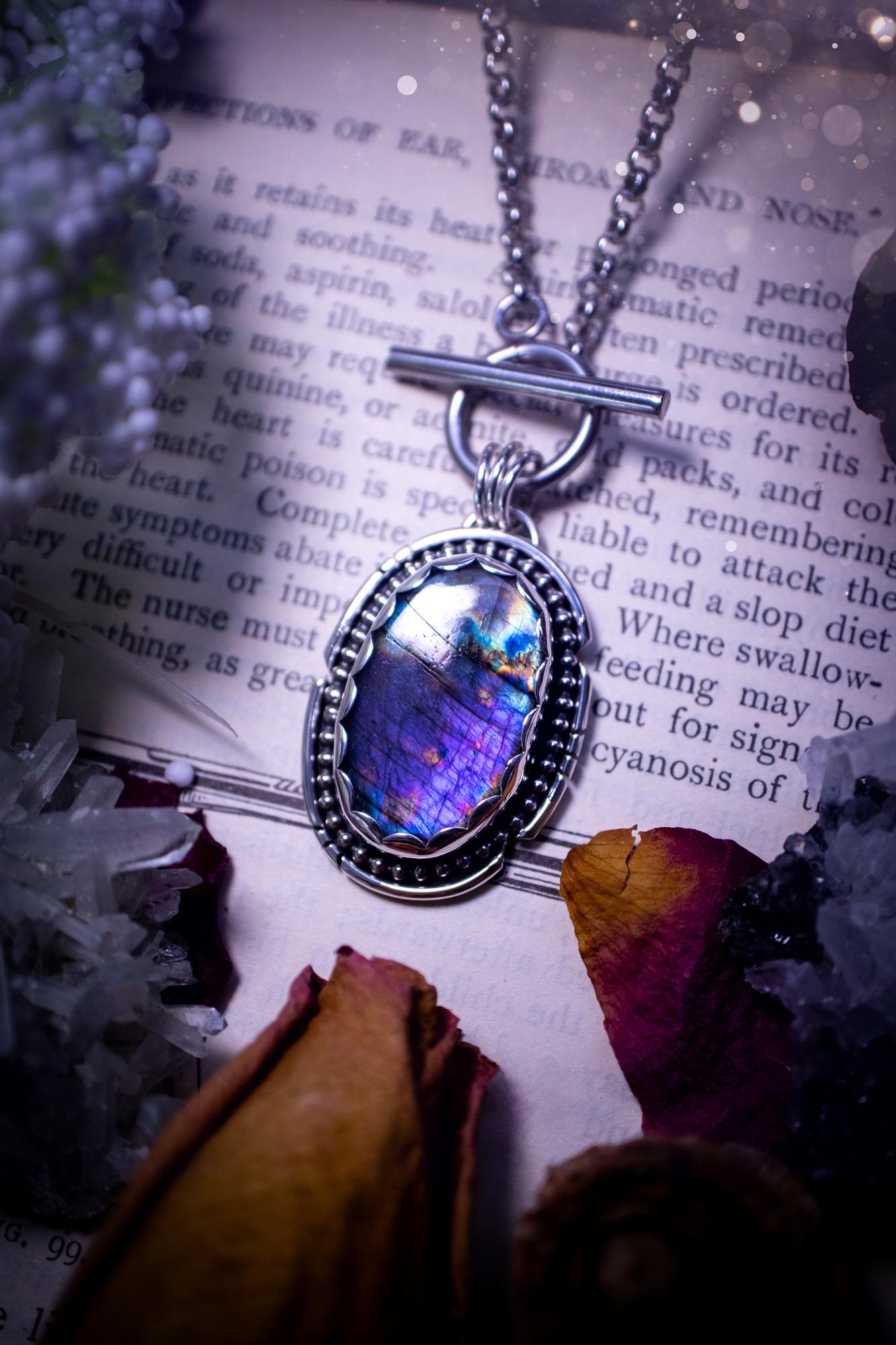 Beautifully handmade, amulet pendant necklace which features the most beautiful rainbow coloured, labradorite spectrolite crystal. This pendant has been handcrafted using a mix of fine and sterling silver. It features a scallop bezel with beaded, and hand carved smooth wire around the stone making this piece totally bespoke and one of a kind. The labradorite has an array of beautiful purples, blues and pinks. This pendant would be suitable for any crystal and jewellery lover, gothic and hippy!