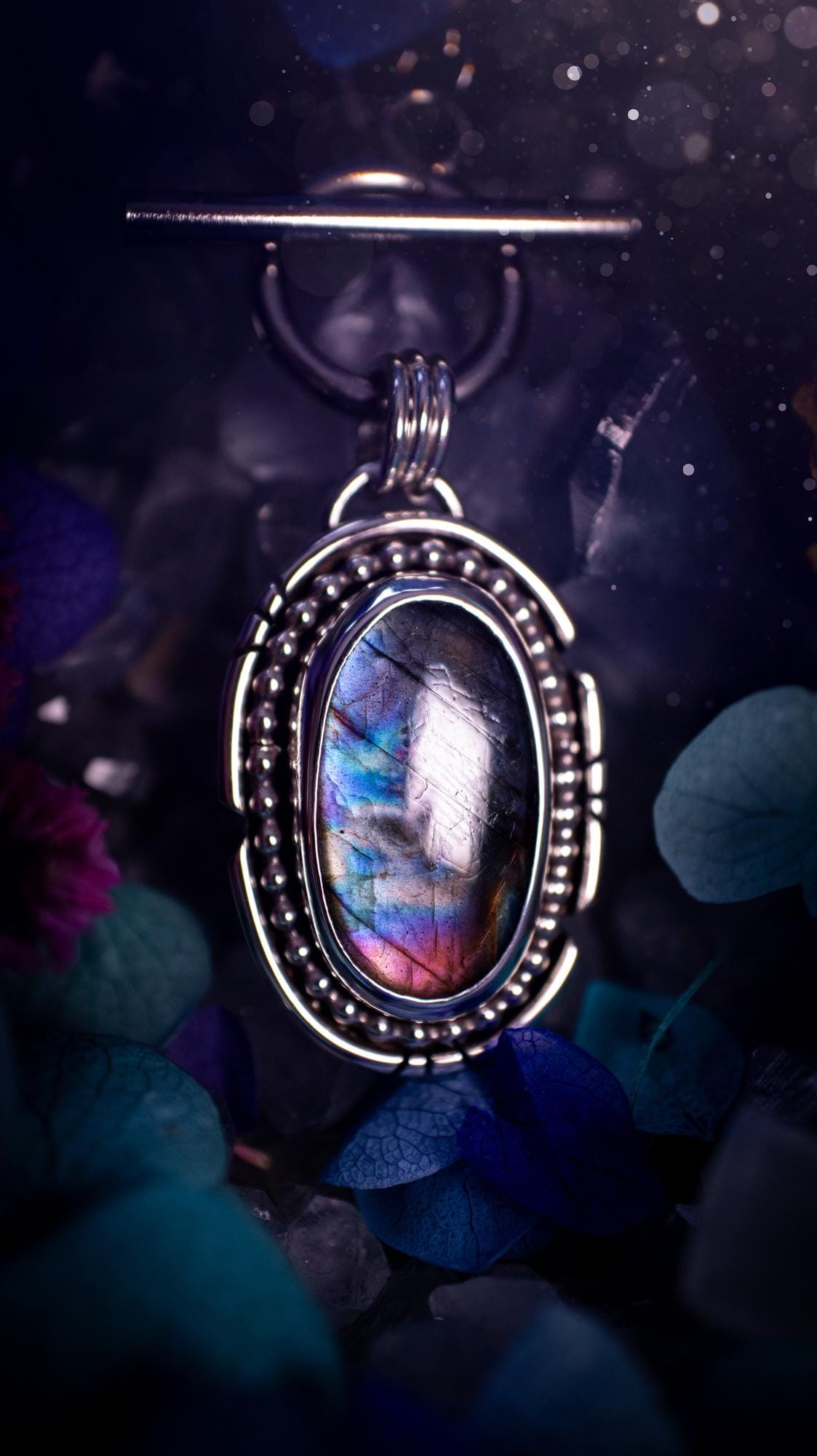 Beautifully handmade, amulet pendant necklace which features the most beautiful rainbow coloured, labradorite spectrolite crystal. This pendant has been handcrafted using a mix of fine and sterling silver. It features a smooth bezel with beaded, and hand carved smooth wire around the stone making this piece totally bespoke and one of a kind. The labradorite has an array of beautiful purples, blues and pinks. This pendant would be suitable for any crystal and jewellery lover, gothic and hippy!