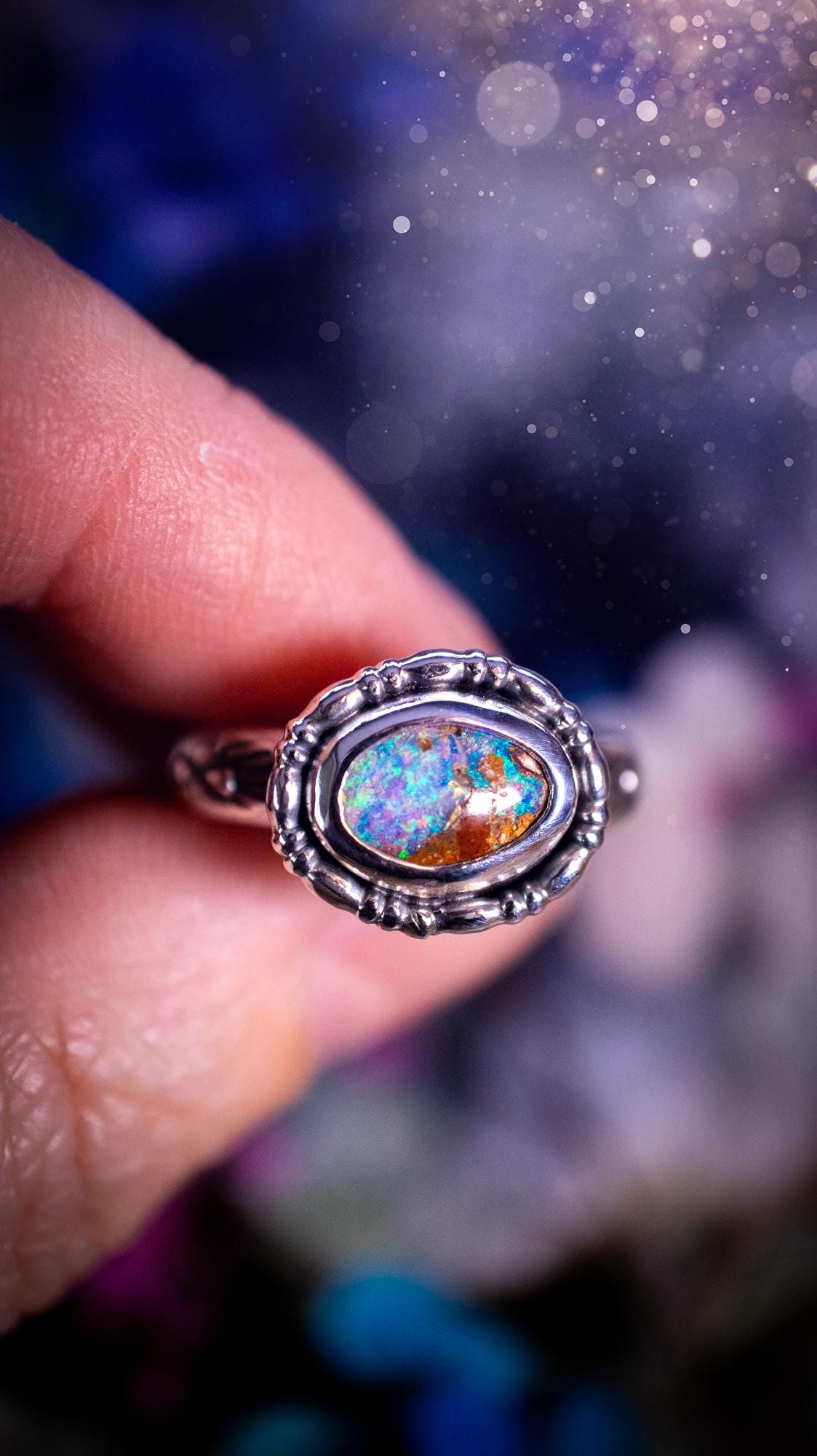 One of a kind and handmade, Australian boulder opal, bohemian ring. This stunning ring has been handcrafted using a mix of fine and sterling silver. Featuring a small, yet totally stunning and vibrant Australian boulder opal full of blues, purples, and green sparkles. Around the smooth bezel is some pretty gallery wire. The ring shank has also been stamped with a bohemian pattern. This one off piece is ideal for any crystal and jewellery lover who is seeking a piece that has no other the same!