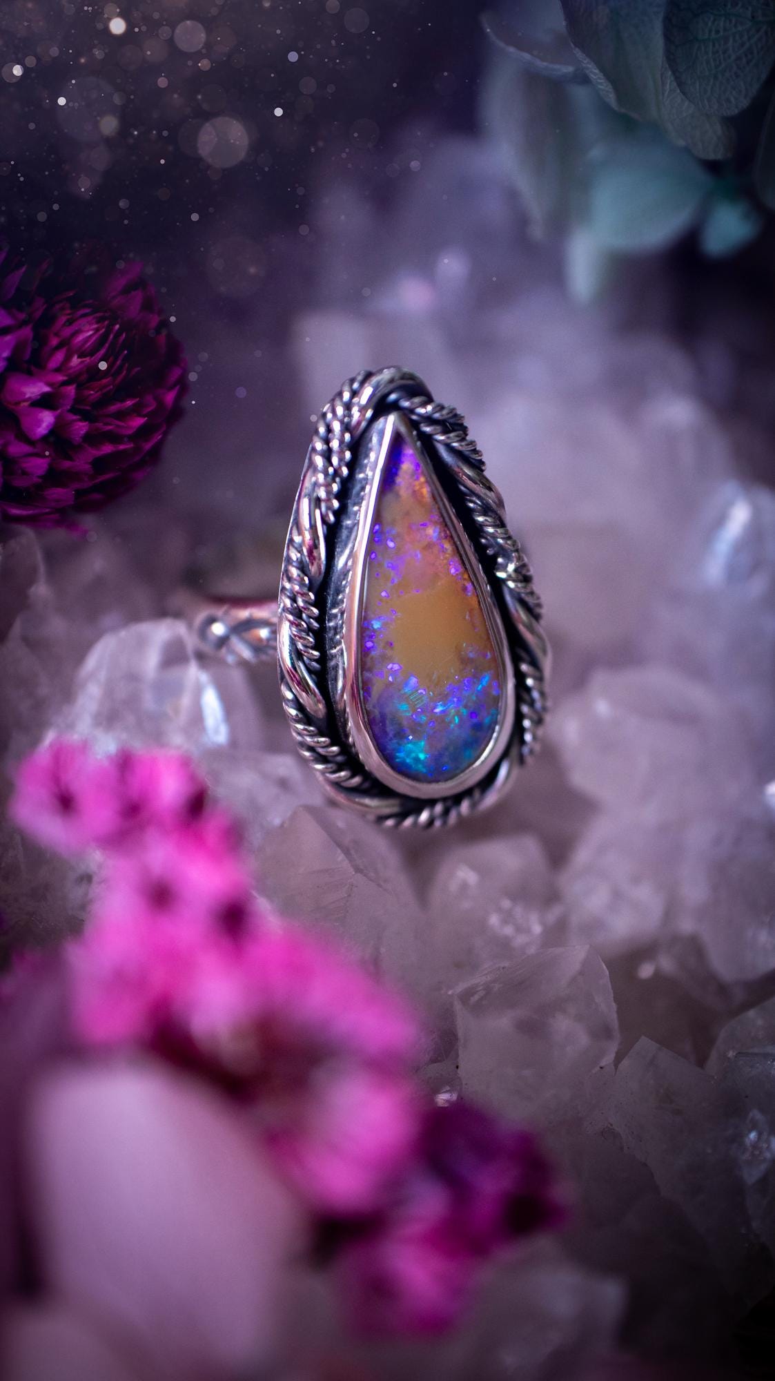 Close-up of a handmade Australian opal ring showing brilliant flashes of pink, blue and purple across the natural gemstone. The opal is securely set in a smooth fine silver bezel with intricate gallery wire detailing beneath. The sterling silver band features a decorative hand-stamped pattern, creating a bold and eye-catching statement ring perfect for opal lovers.