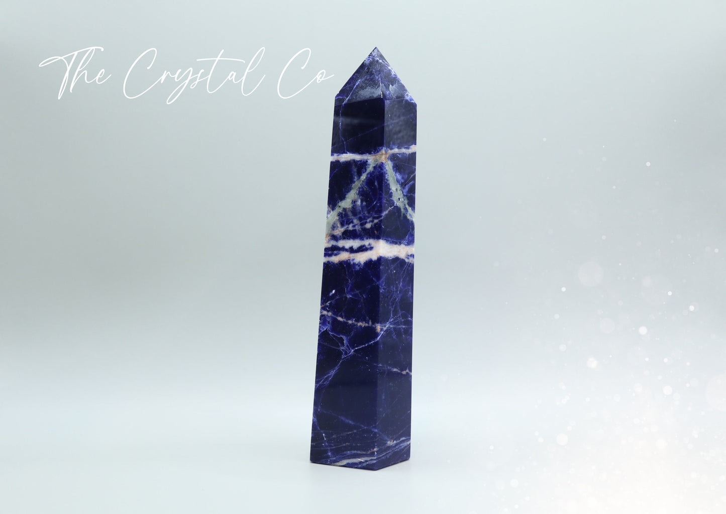 Sodalite crystal tower with deep blue hues and natural white veins. Polished to a smooth finish, standing upright with a pointed top. Perfect for home decor, meditation, or crystal collections. Unique and eye-catching, showcasing its natural beauty.