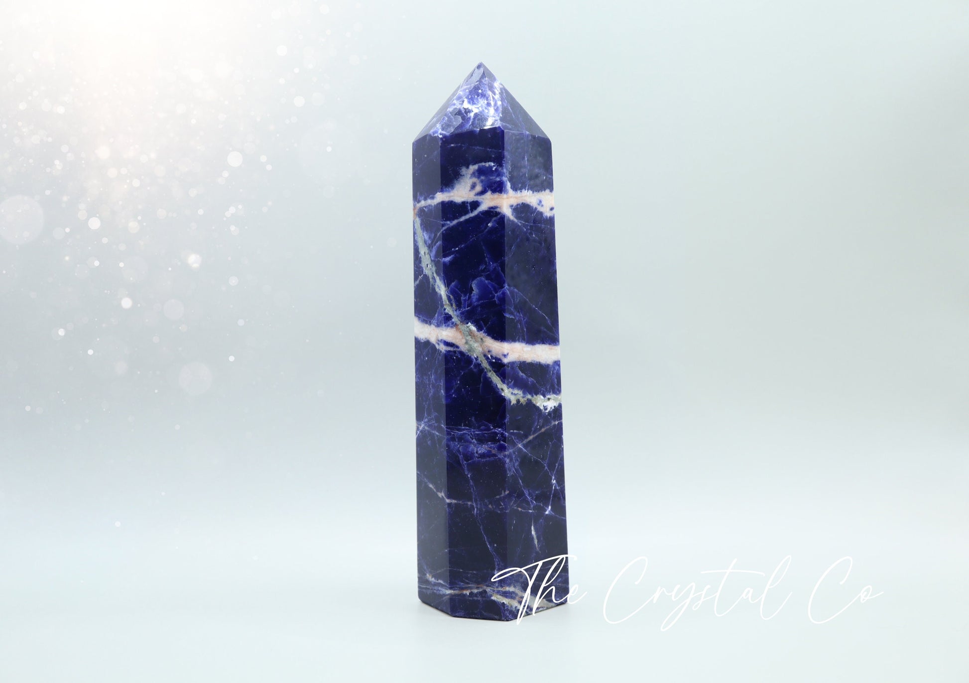 Large sodalite crystal tower with deep blue hues and striking white veining, standing upright on a smooth, polished base. Perfect as a statement piece for home decor, meditation, or crystal collections. Handmade to showcase its natural beauty.