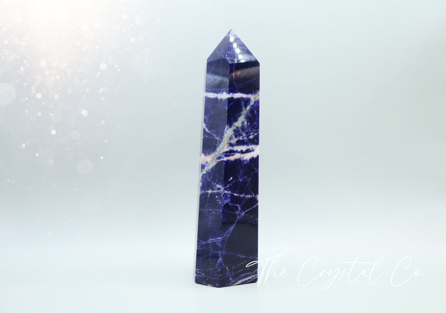 Sodalite crystal tower with deep blue hues and natural white veins. Polished to a smooth finish, standing upright with a pointed top. Perfect for home decor, meditation, or crystal collections. Unique and eye-catching, showcasing its natural beauty.