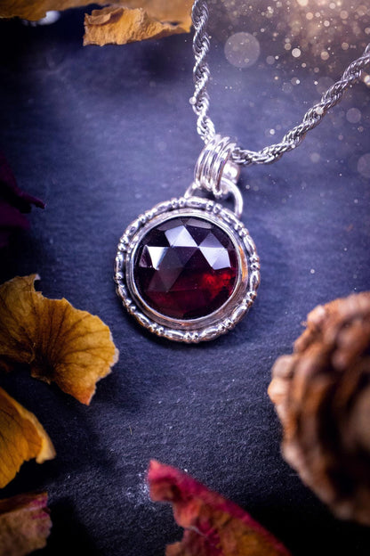 Handmade sterling silver pendant necklace featuring a circular design with a deep red garnet crystal centrepiece, showcasing a minimalist yet elegant artisan style. This piece has been created using recycled fine and sterling silver and features a gorgeous rose cut garnet that is full of sparkle. Suitable or special occasions such as birthdays, anniversaries, graduations and more. Garnet is the birthstone for January. Witchy and gothic handmade jewellery.