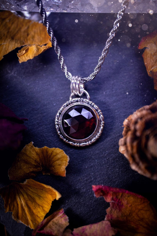 Handmade sterling silver pendant necklace featuring a circular design with a deep red garnet crystal centrepiece, showcasing a minimalist yet elegant artisan style. This piece has been created using recycled fine and sterling silver and features a gorgeous rose cut garnet that is full of sparkle. Suitable or special occasions such as birthdays, anniversaries, graduations and more. Garnet is the birthstone for January. Witchy and gothic handmade jewellery.