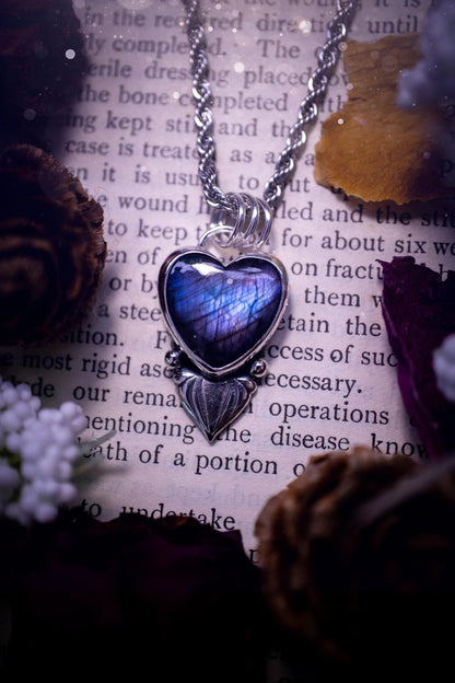 Stunning and handmade, all natural, purple and blue, labradorite crystal heart pendant necklace. This pendant necklace has been handmade from fine and sterling silver. Featuring the most beautiful labradorite heart crystal that is full of bold purples, deep blues and a shimmer of silver. Accompanying the crystal gemstone is fan and ball silver components giving this piece its own uniqueness. This piece of jewellery would be ideal for any crystal or jewellery lover and gives off gothic vibes.
