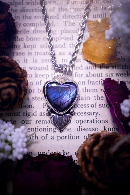 Stunning and handmade, all natural, purple and blue, labradorite crystal heart pendant necklace. This pendant necklace has been handmade from fine and sterling silver. Featuring the most beautiful labradorite heart crystal that is full of bold purples, deep blues and a shimmer of silver. Accompanying the crystal gemstone is fan and ball silver components giving this piece its own uniqueness. This piece of jewellery would be ideal for any crystal or jewellery lover and gives off gothic vibes.
