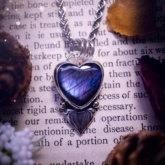 Stunning and handmade, all natural, purple and blue, labradorite crystal heart pendant necklace. This pendant necklace has been handmade from fine and sterling silver. Featuring the most beautiful labradorite heart crystal that is full of bold purples, deep blues and a shimmer of silver. Accompanying the crystal gemstone is fan and ball silver components giving this piece its own uniqueness. This piece of jewellery would be ideal for any crystal or jewellery lover and gives off gothic vibes.