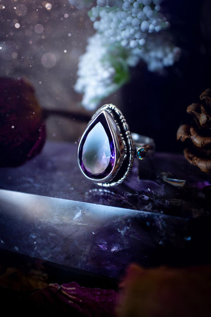 Handmade statement ring crafted from sterling silver in a striking gothic design. This bold piece features a stunning faceted amethyst as the central gemstone, radiating rich purple hues. Flanking the amethyst are sparkling aurora cubic zirconia, that catch the light with a dazzling iridescence. The intricate detailing and dark romantic style give the ring a mystical feel, perfect for lovers of gothic, or alternative jewelry. Unique and eye-catching, this ring makes a powerful, meaningful gift.