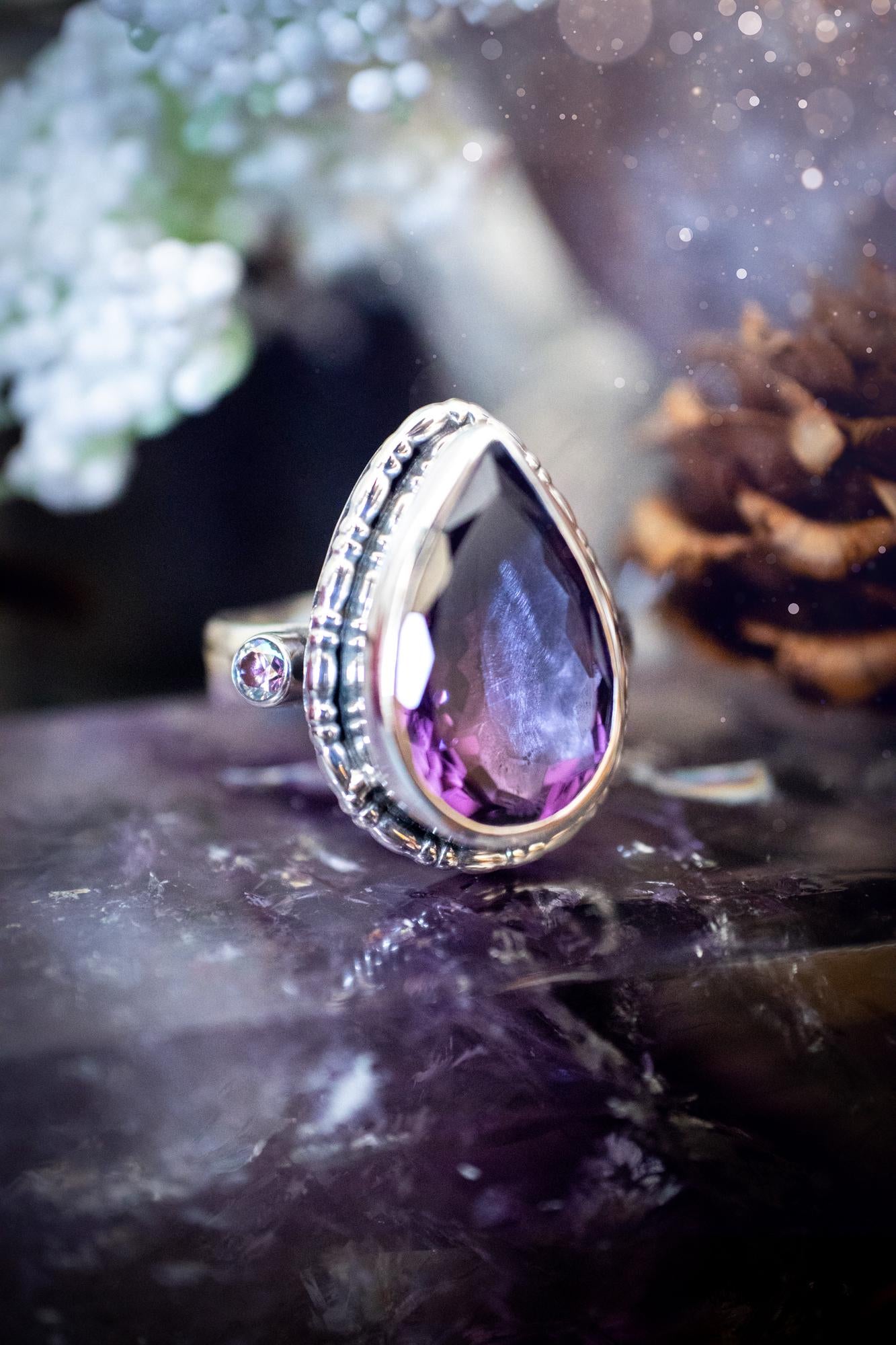 Handmade statement ring crafted from sterling silver in a striking gothic design. This bold piece features a stunning faceted amethyst as the central gemstone, radiating rich purple hues. Flanking the amethyst are sparkling aurora cubic zirconia, that catch the light with a dazzling iridescence. The intricate detailing and dark romantic style give the ring a mystical feel, perfect for lovers of gothic, or alternative jewelry. Unique and eye-catching, this ring makes a powerful, meaningful gift.