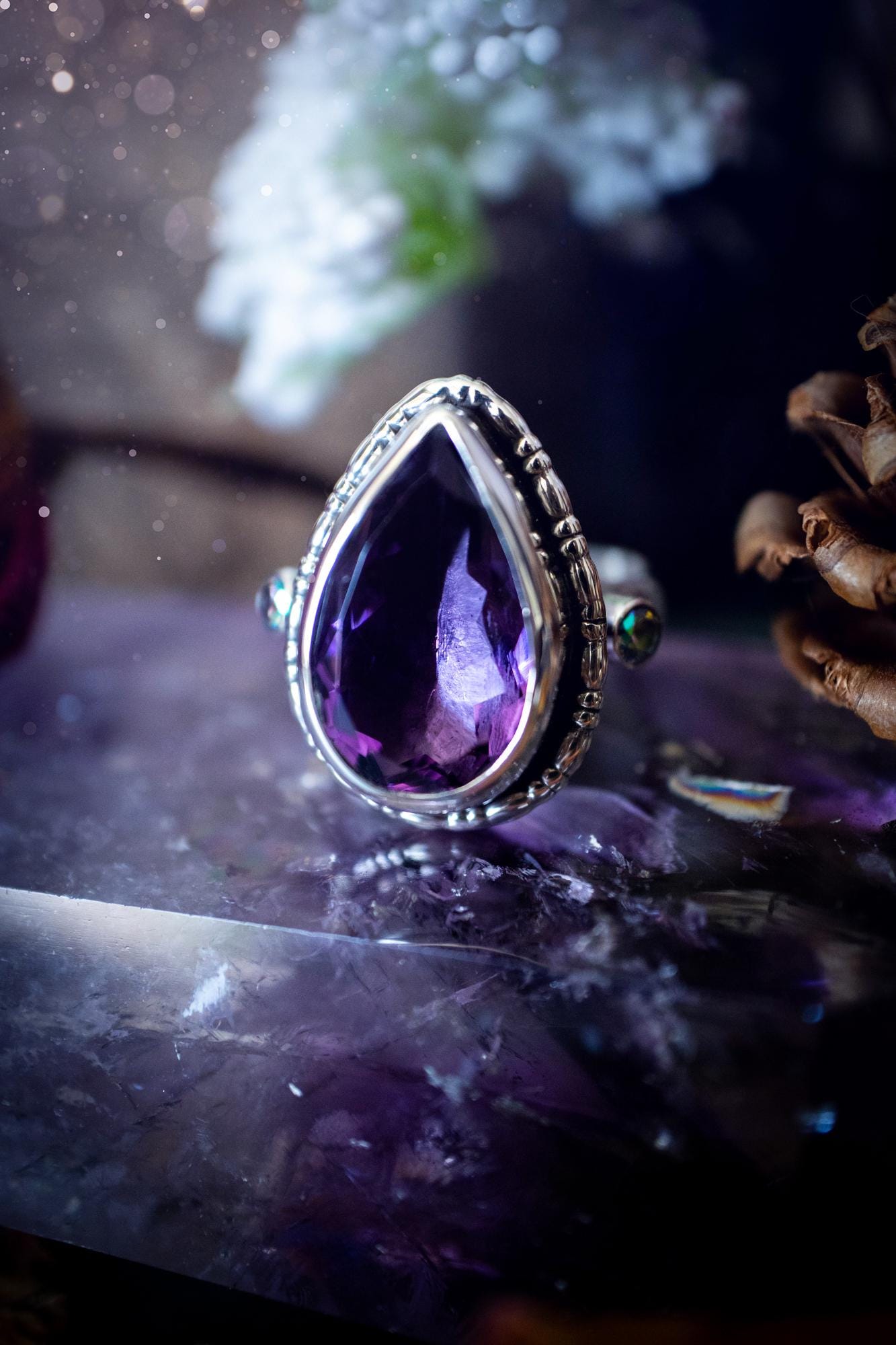 Handmade statement ring crafted from sterling silver in a striking gothic design. This bold piece features a stunning faceted amethyst as the central gemstone, radiating rich purple hues. Flanking the amethyst are sparkling aurora cubic zirconia, that catch the light with a dazzling iridescence. The intricate detailing and dark romantic style give the ring a mystical feel, perfect for lovers of gothic, or alternative jewelry. Unique and eye-catching, this ring makes a powerful, meaningful gift.