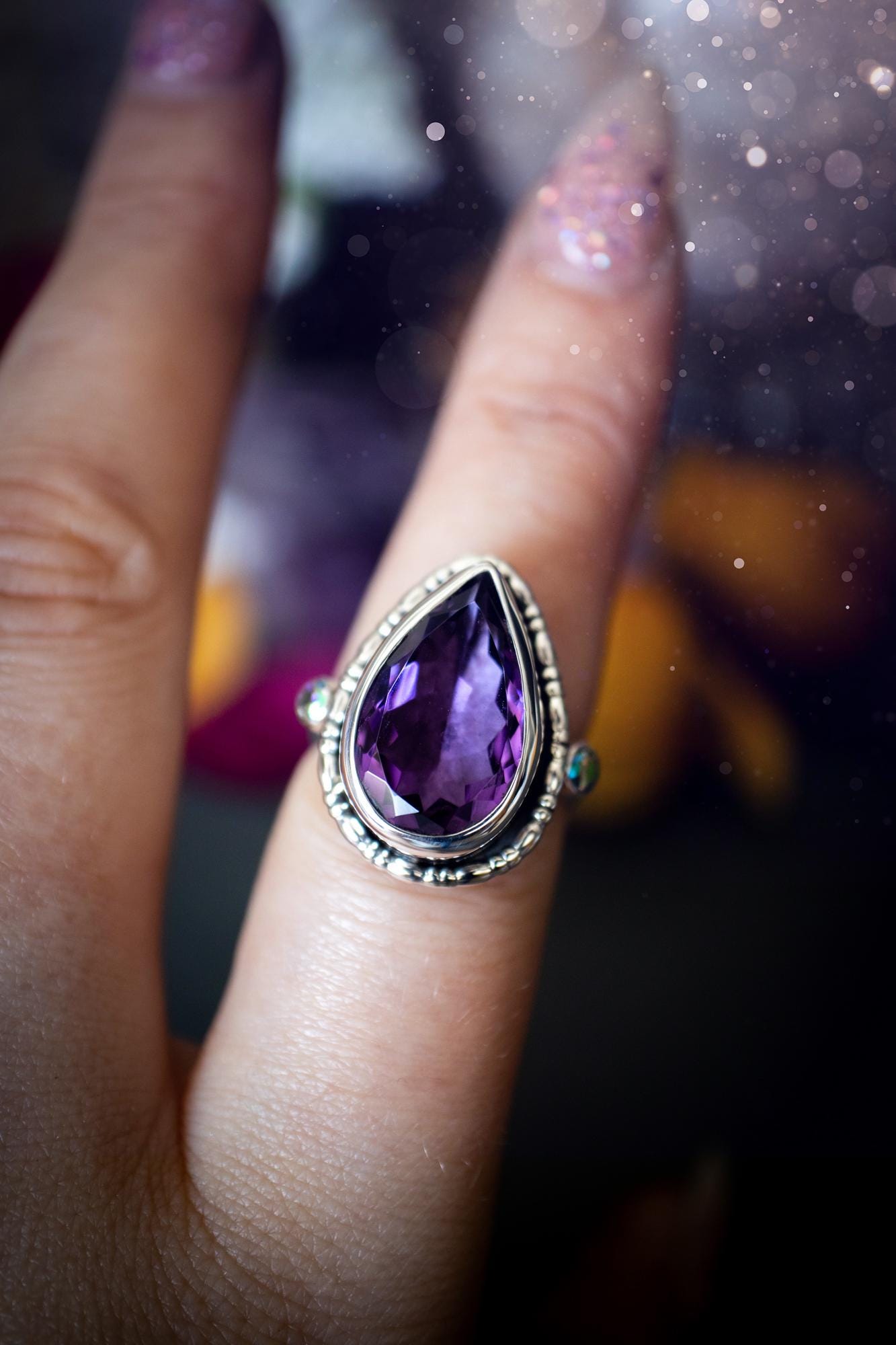 Handmade statement ring crafted from sterling silver in a striking gothic design. This bold piece features a stunning faceted amethyst as the central gemstone, radiating rich purple hues. Flanking the amethyst are sparkling aurora cubic zirconia, that catch the light with a dazzling iridescence. The intricate detailing and dark romantic style give the ring a mystical feel, perfect for lovers of gothic, or alternative jewelry. Unique and eye-catching, this ring makes a powerful, meaningful gift.