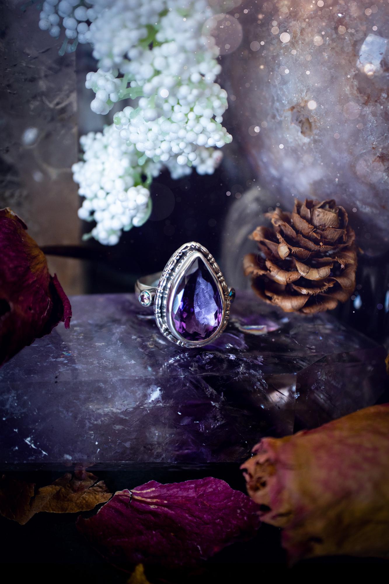 Handmade statement ring crafted from sterling silver in a striking gothic design. This bold piece features a stunning faceted amethyst as the central gemstone, radiating rich purple hues. Flanking the amethyst are sparkling aurora cubic zirconia, that catch the light with a dazzling iridescence. The intricate detailing and dark romantic style give the ring a mystical feel, perfect for lovers of gothic, or alternative jewelry. Unique and eye-catching, this ring makes a powerful, meaningful gift.