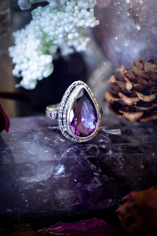 Handmade statement ring crafted from sterling silver in a striking gothic design. This bold piece features a stunning faceted amethyst as the central gemstone, radiating rich purple hues. Flanking the amethyst are sparkling aurora cubic zirconia, that catch the light with a dazzling iridescence. The intricate detailing and dark romantic style give the ring a mystical feel, perfect for lovers of gothic, or alternative jewelry. Unique and eye-catching, this ring makes a powerful, meaningful gift.