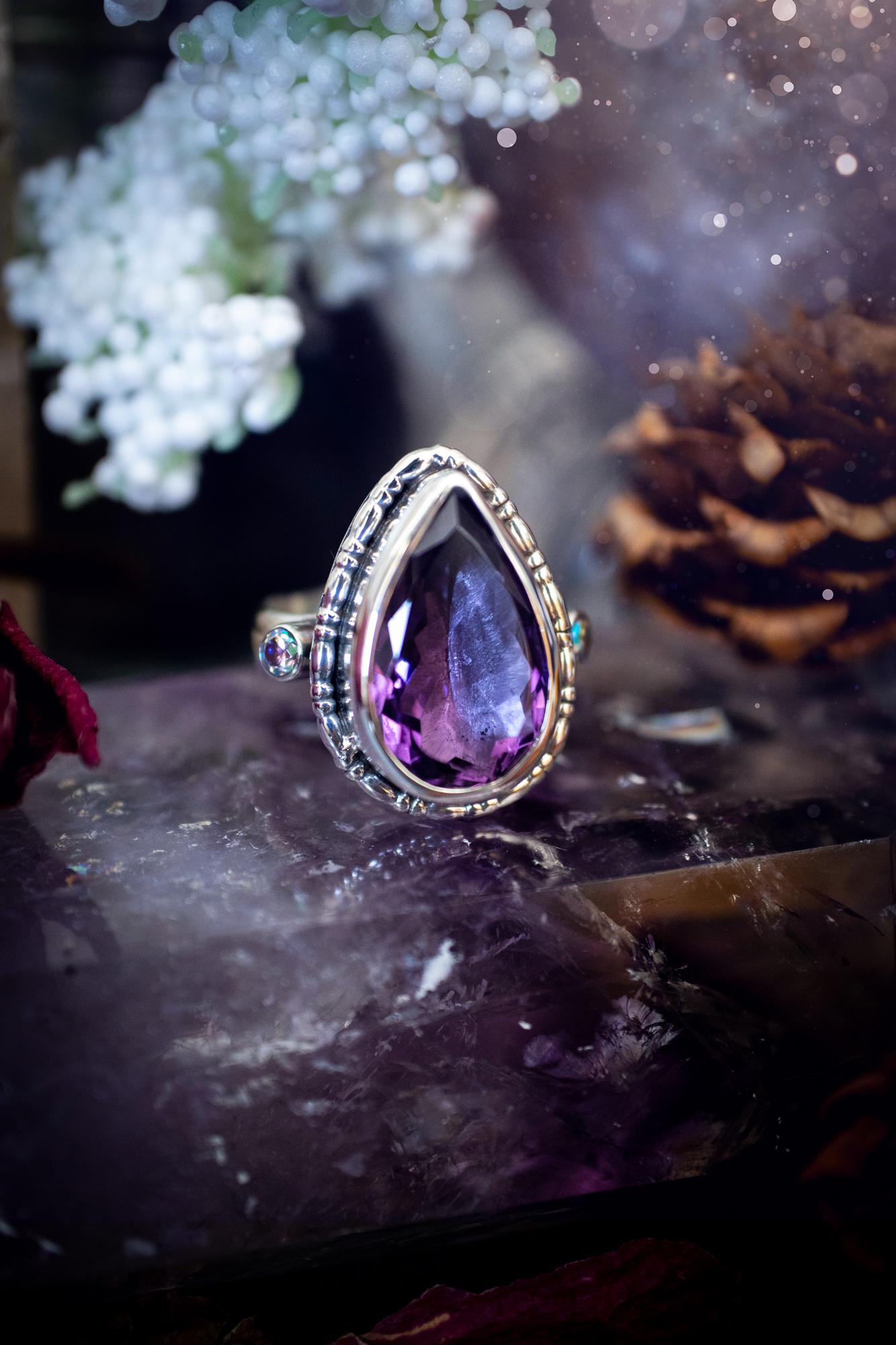 Handmade statement ring crafted from sterling silver in a striking gothic design. This bold piece features a stunning faceted amethyst as the central gemstone, radiating rich purple hues. Flanking the amethyst are sparkling aurora cubic zirconia, that catch the light with a dazzling iridescence. The intricate detailing and dark romantic style give the ring a mystical feel, perfect for lovers of gothic, or alternative jewelry. Unique and eye-catching, this ring makes a powerful, meaningful gift.