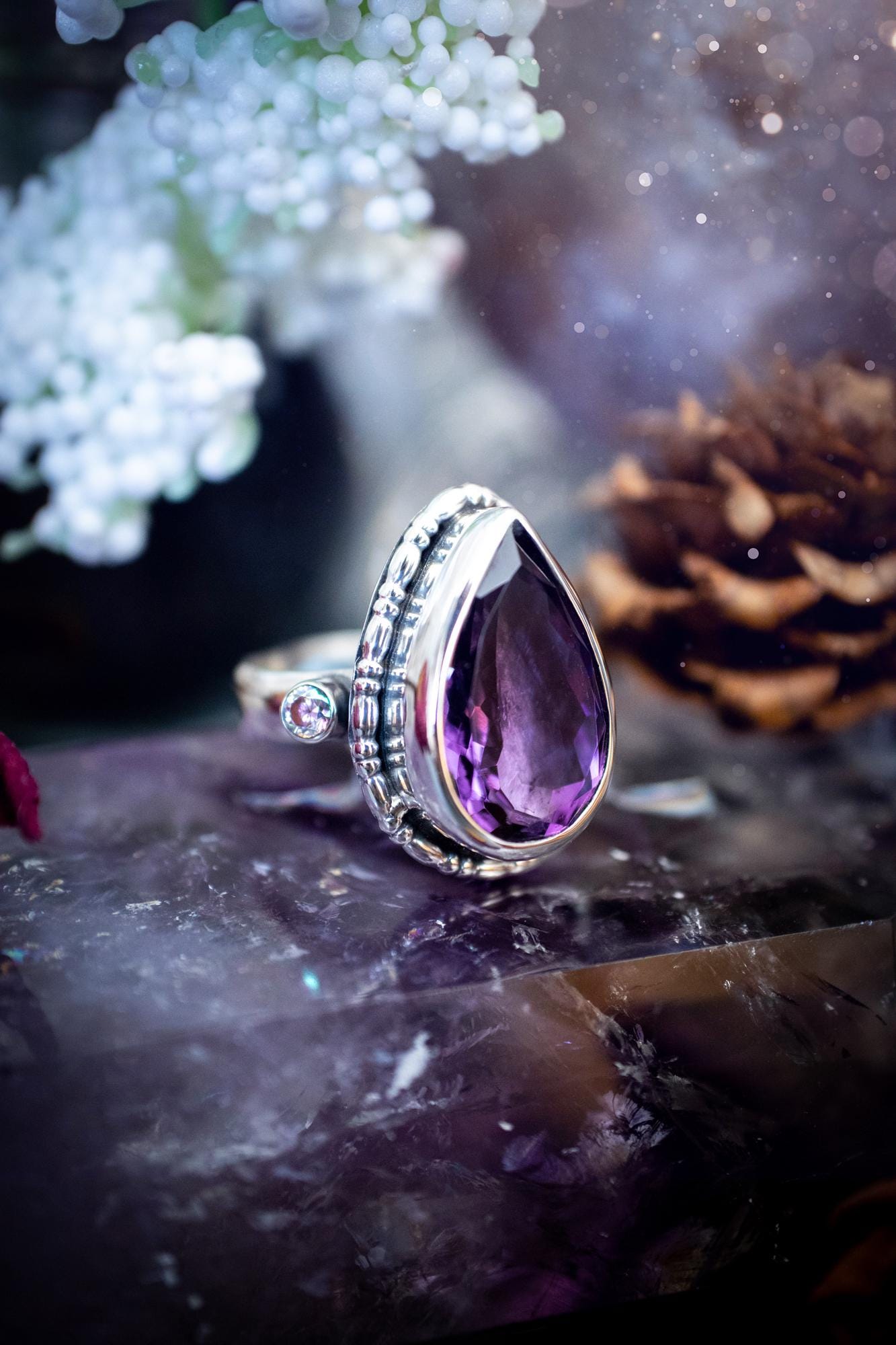 Handmade statement ring crafted from sterling silver in a striking gothic design. This bold piece features a stunning faceted amethyst as the central gemstone, radiating rich purple hues. Flanking the amethyst are sparkling aurora cubic zirconia, that catch the light with a dazzling iridescence. The intricate detailing and dark romantic style give the ring a mystical feel, perfect for lovers of gothic, or alternative jewelry. Unique and eye-catching, this ring makes a powerful, meaningful gift.