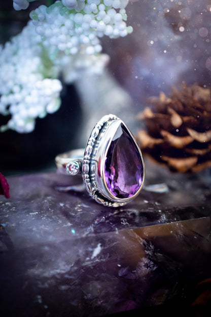 Handmade statement ring crafted from sterling silver in a striking gothic design. This bold piece features a stunning faceted amethyst as the central gemstone, radiating rich purple hues. Flanking the amethyst are sparkling aurora cubic zirconia, that catch the light with a dazzling iridescence. The intricate detailing and dark romantic style give the ring a mystical feel, perfect for lovers of gothic, or alternative jewelry. Unique and eye-catching, this ring makes a powerful, meaningful gift.