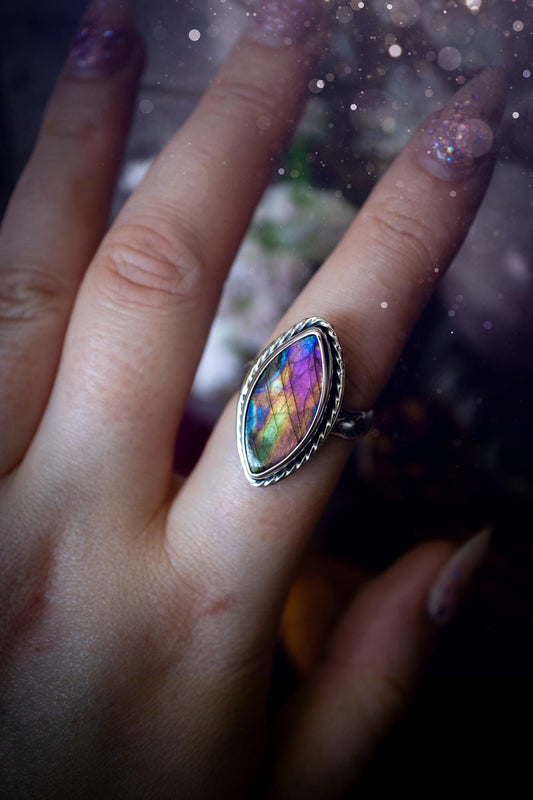 Handcrafted sterling silver statement ring featuring a stunning spectrolite labradorite crystal with vibrant flashes of purple, pink, and orange. This magical gemstone shimmers with an ethereal glow, making it a captivating piece for any jewellery collection. Ideal for crystal lovers, spiritual souls, and those drawn to unique, one-of-a-kind designs. A bold, mystical accessory perfect for expressing your inner light and energy. Gothic and handmade jewellery gifts, ideal for crystal lovers.
