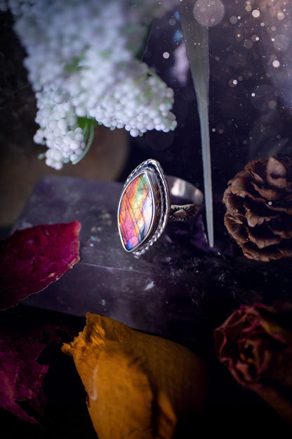 Handcrafted sterling silver statement ring featuring a stunning spectrolite labradorite crystal with vibrant flashes of purple, pink, and orange. This magical gemstone shimmers with an ethereal glow, making it a captivating piece for any jewellery collection. Ideal for crystal lovers, spiritual souls, and those drawn to unique, one-of-a-kind designs. A bold, mystical accessory perfect for expressing your inner light and energy. Gothic and handmade jewellery gifts, ideal for crystal lovers.