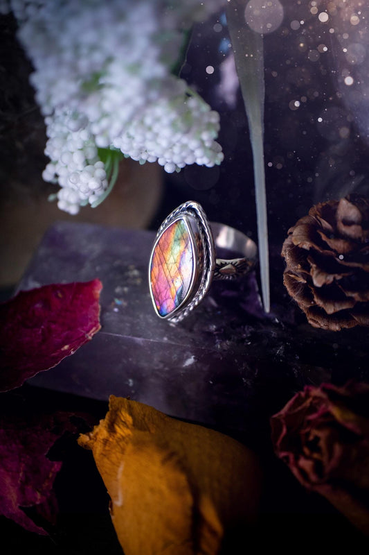Handcrafted sterling silver statement ring featuring a stunning spectrolite labradorite crystal with vibrant flashes of purple, pink, and orange. This magical gemstone shimmers with an ethereal glow, making it a captivating piece for any jewellery collection. Ideal for crystal lovers, spiritual souls, and those drawn to unique, one-of-a-kind designs. A bold, mystical accessory perfect for expressing your inner light and energy. Gothic and handmade jewellery gifts, ideal for crystal lovers.