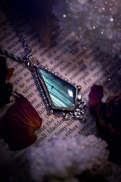This stunning pendant necklace has been handcrafted using a mix of recycled fine and sterling silver. Featuring a beautiful and natural green and blue hued labradorite crystal that is full of flash! accompanying this magical crystal is a mix of fae inspired components such as little leaves, flower, silver balls and gothic gallery wire. A true bespoke piece with no other being the same! Ideal for any crystal and jewellery lover that loves a witchy and gothic vibe, along with the beauty of nature!