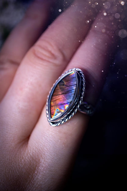 Handcrafted sterling silver statement ring featuring a stunning spectrolite labradorite crystal with vibrant flashes of purple, pink, and orange. This magical gemstone shimmers with an ethereal glow, making it a captivating piece for any jewellery collection. Ideal for crystal lovers, spiritual souls, and those drawn to unique, one-of-a-kind designs. A bold, mystical accessory perfect for expressing your inner light and energy. Gothic and handmade jewellery gifts, ideal for crystal lovers.
