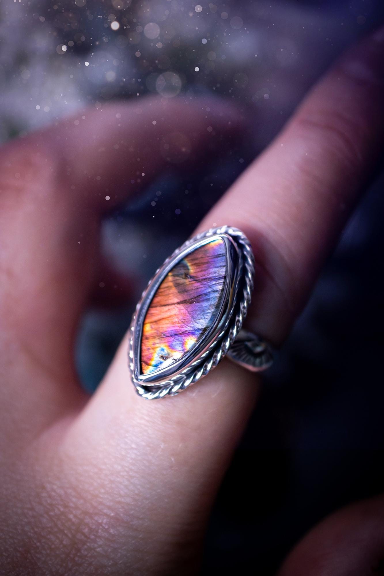 Handcrafted sterling silver statement ring featuring a stunning spectrolite labradorite crystal with vibrant flashes of purple, pink, and orange. This magical gemstone shimmers with an ethereal glow, making it a captivating piece for any jewellery collection. Ideal for crystal lovers, spiritual souls, and those drawn to unique, one-of-a-kind designs. A bold, mystical accessory perfect for expressing your inner light and energy. Gothic and handmade jewellery gifts, ideal for crystal lovers.