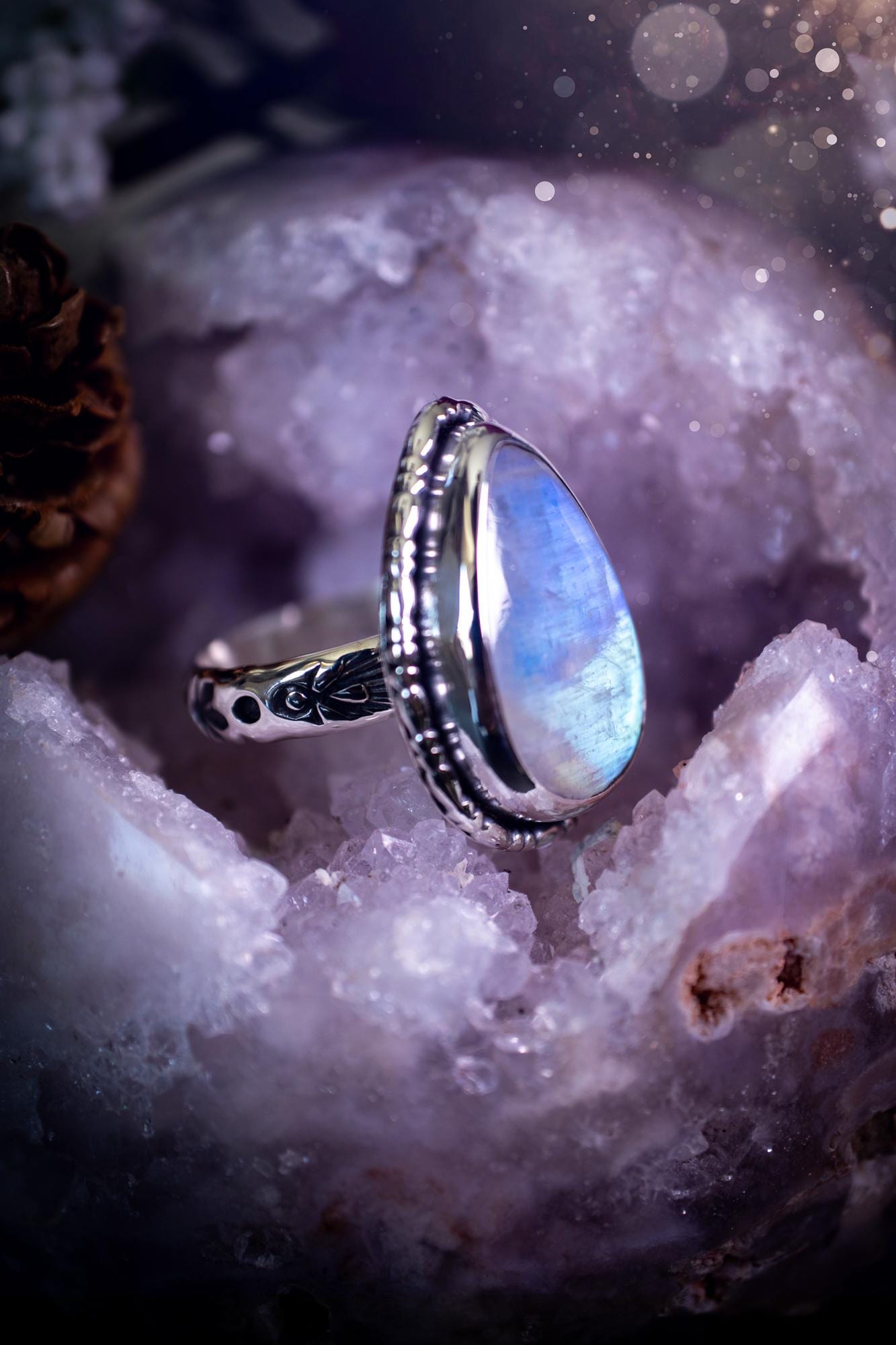 A handcrafted rainbow moonstone statement ring with a large, iridescent gemstone glowing with blue and purple flashes. The design blends gothic and whimsical &quot;hoppy&quot; vibes, with bespoke stamping etched into the sterling and fine silver shank. The silver band features intricate detailing, adding texture and character, while the moonstone is bezel-set, enhancing its mystical, ethereal aura. A bold and unique artisan piece with personalized charm. Ideal for crystal and jewellery lovers, h