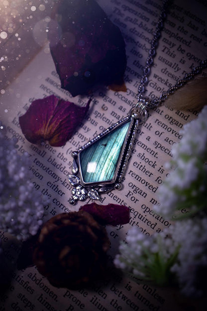 This stunning pendant necklace has been handcrafted using a mix of recycled fine and sterling silver. Featuring a beautiful and natural green and blue hued labradorite crystal that is full of flash! accompanying this magical crystal is a mix of fae inspired components such as little leaves, flower, silver balls and gothic gallery wire. A true bespoke piece with no other being the same! Ideal for any crystal and jewellery lover that loves a witchy and gothic vibe, along with the beauty of nature!