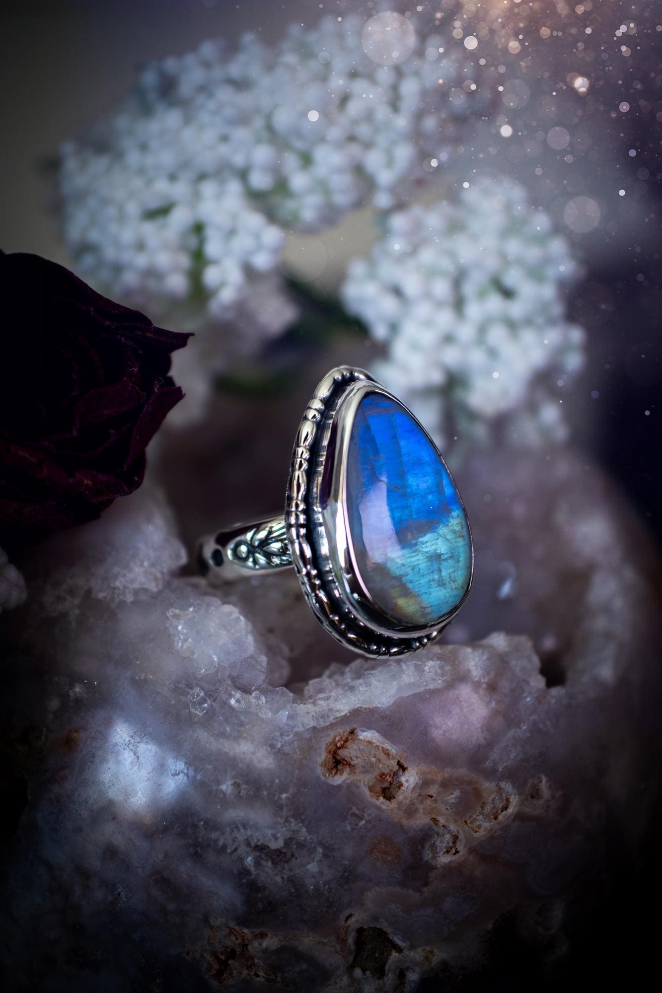 A handcrafted rainbow moonstone statement ring with a large, iridescent gemstone glowing with blue and purple flashes. The design blends gothic and whimsical &quot;hoppy&quot; vibes, with bespoke stamping etched into the sterling and fine silver shank. The silver band features intricate detailing, adding texture and character, while the moonstone is bezel-set, enhancing its mystical, ethereal aura. A bold and unique artisan piece with personalized charm. Ideal for crystal and jewellery lovers, h