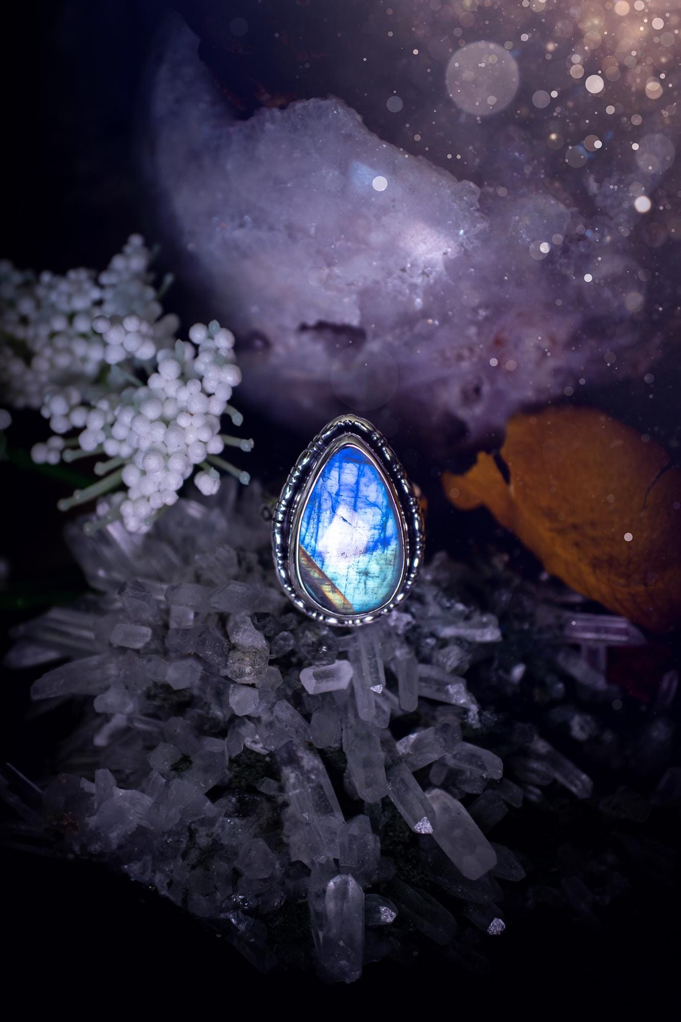 A handcrafted rainbow moonstone statement ring with a large, iridescent gemstone glowing with blue and purple flashes. The design blends gothic and whimsical &quot;hoppy&quot; vibes, with bespoke stamping etched into the sterling and fine silver shank. The silver band features intricate detailing, adding texture and character, while the moonstone is bezel-set, enhancing its mystical, ethereal aura. A bold and unique artisan piece with personalized charm. Ideal for crystal and jewellery lovers, h