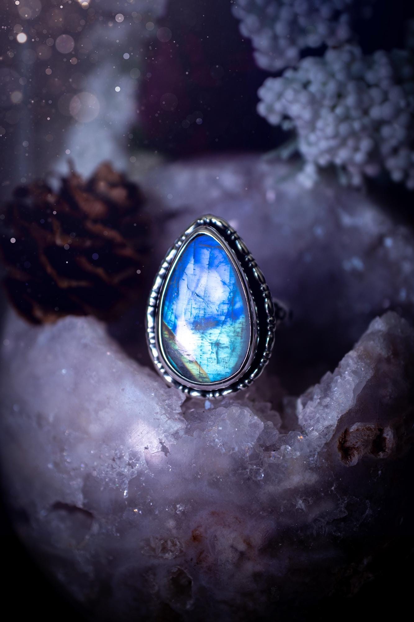 A handcrafted rainbow moonstone statement ring with a large, iridescent gemstone glowing with blue and purple flashes. The design blends gothic and whimsical &quot;hoppy&quot; vibes, with bespoke stamping etched into the sterling and fine silver shank. The silver band features intricate detailing, adding texture and character, while the moonstone is bezel-set, enhancing its mystical, ethereal aura. A bold and unique artisan piece with personalized charm. Ideal for crystal and jewellery lovers, h