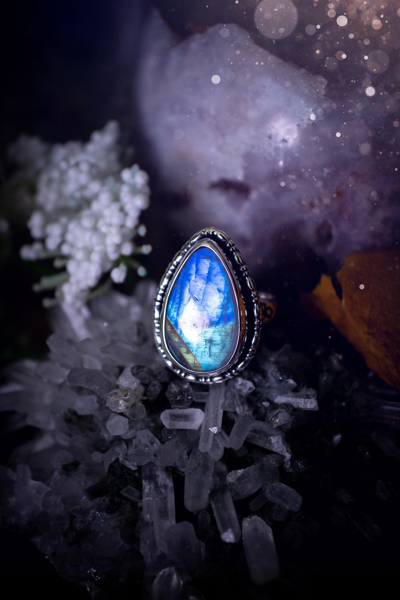 A handcrafted rainbow moonstone statement ring with a large, iridescent gemstone glowing with blue and purple flashes. The design blends gothic and whimsical &quot;hoppy&quot; vibes, with bespoke stamping etched into the sterling and fine silver shank. The silver band features intricate detailing, adding texture and character, while the moonstone is bezel-set, enhancing its mystical, ethereal aura. A bold and unique artisan piece with personalized charm. Ideal for crystal and jewellery lovers, h