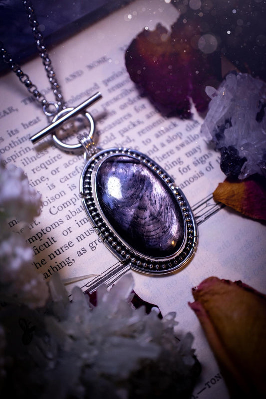 Beautifully handmade, amulet pendant necklace which features the most beautiful, flashy hypersthene crystal gemstone. This pendant has been handcrafted using a mix of fine and sterling silver. It features a smooth bezel with beaded, and hand carved smooth wire around the stone making this piece totally bespoke and one of a kind. The hypersthene has an array of beautiful greys and blacks. This pendant would be suitable for any crystal and jewellery lover, full of gothic and witchy vibes.
