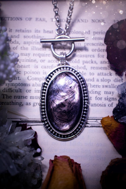 Beautifully handmade, amulet pendant necklace which features the most beautiful, flashy hypersthene crystal gemstone. This pendant has been handcrafted using a mix of fine and sterling silver. It features a smooth bezel with beaded, and hand carved smooth wire around the stone making this piece totally bespoke and one of a kind. The hypersthene has an array of beautiful greys and blacks. This pendant would be suitable for any crystal and jewellery lover, full of gothic and witchy vibes.