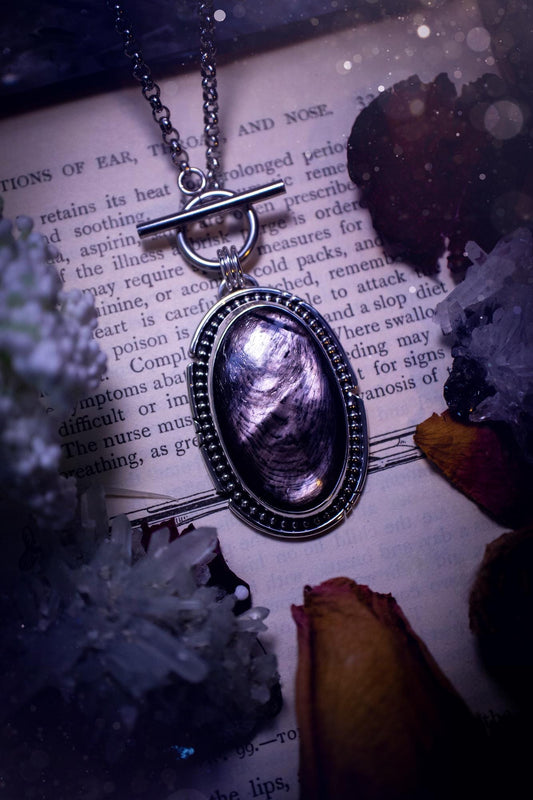 Beautifully handmade, amulet pendant necklace which features the most beautiful, flashy hypersthene crystal gemstone. This pendant has been handcrafted using a mix of fine and sterling silver. It features a smooth bezel with beaded, and hand carved smooth wire around the stone making this piece totally bespoke and one of a kind. The hypersthene has an array of beautiful greys and blacks. This pendant would be suitable for any crystal and jewellery lover, full of gothic and witchy vibes.