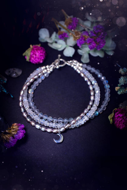 Stunning and handcrafted, triple crystal beaded bracelet. This beautiful bracelet consists of three bracelets in one all held together with a sterling silver t-bar toggle clasp. Featuring stunning flashy rainbow moonstone, light coloured labradorite, and grey to purple fresh water pearls. The findings on this bracelet are sterling silver, with a stainless steel moon charm. This piece is totally bespoke and full of celestial vibes. Ideal for any crystal and jewellery lover. Witchy and gothic