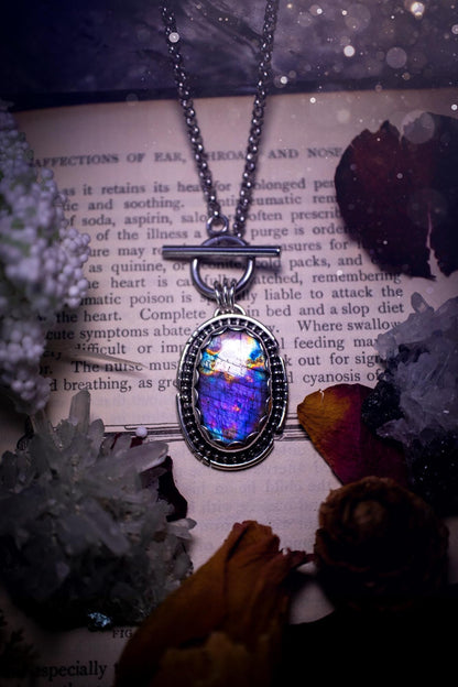Beautifully handmade, amulet pendant necklace which features the most beautiful rainbow coloured, labradorite spectrolite crystal. This pendant has been handcrafted using a mix of fine and sterling silver. It features a scallop bezel with beaded, and hand carved smooth wire around the stone making this piece totally bespoke and one of a kind. The labradorite has an array of beautiful purples, blues and pinks. This pendant would be suitable for any crystal and jewellery lover, gothic and hippy!