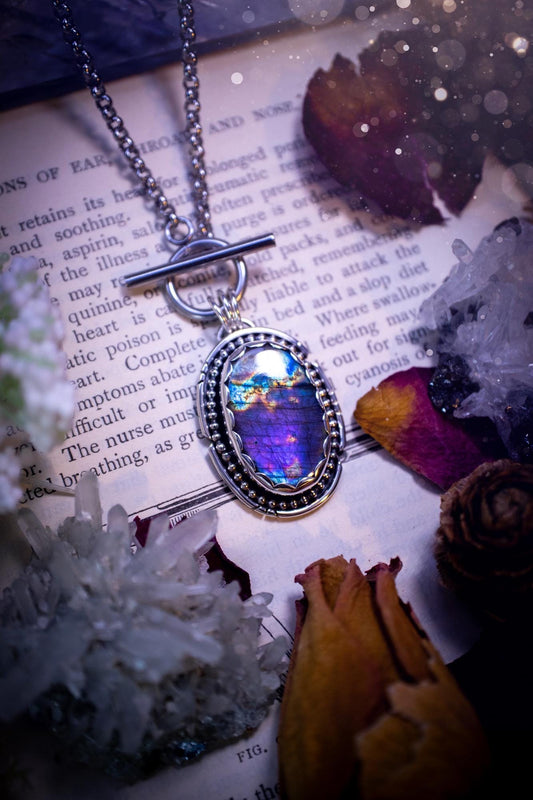 Beautifully handmade, amulet pendant necklace which features the most beautiful rainbow coloured, labradorite spectrolite crystal. This pendant has been handcrafted using a mix of fine and sterling silver. It features a scallop bezel with beaded, and hand carved smooth wire around the stone making this piece totally bespoke and one of a kind. The labradorite has an array of beautiful purples, blues and pinks. This pendant would be suitable for any crystal and jewellery lover, gothic and hippy!