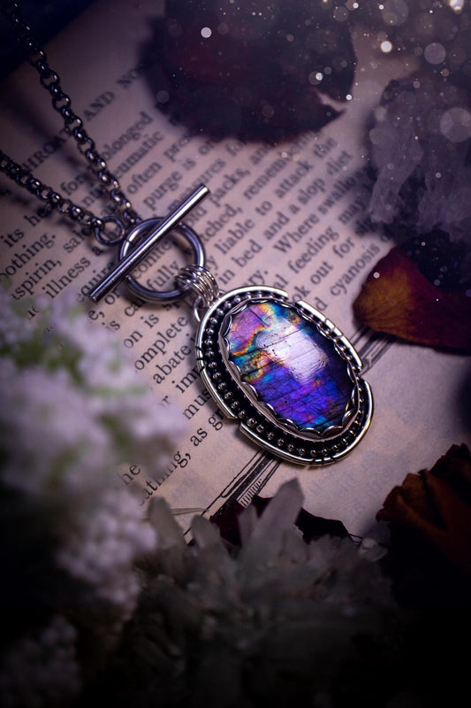 Beautifully handmade, amulet pendant necklace which features the most beautiful rainbow coloured, labradorite spectrolite crystal. This pendant has been handcrafted using a mix of fine and sterling silver. It features a scallop bezel with beaded, and hand carved smooth wire around the stone making this piece totally bespoke and one of a kind. The labradorite has an array of beautiful purples, blues and pinks. This pendant would be suitable for any crystal and jewellery lover, gothic and hippy!