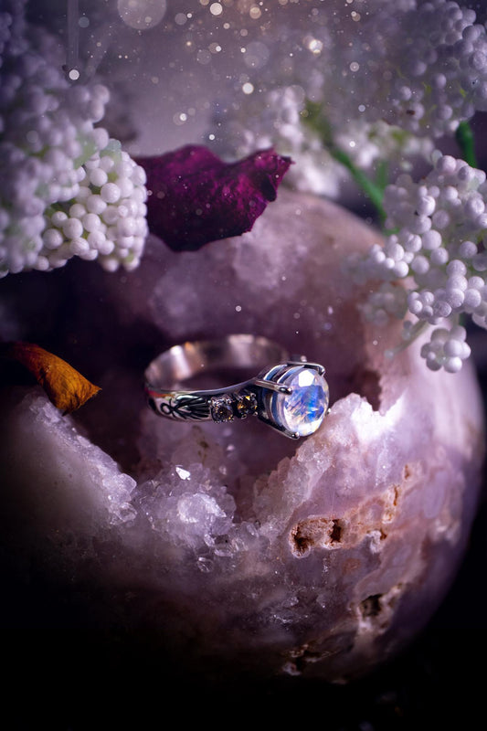 Beautifully handmade, and bespoke, natural rainbow moonstone statement ring. This one of a kind ring has been handmade using a mix of fine and sterling silver. Featuring a beautiful, flashy round, natural rainbow moonstone crystal that has stunning hues of blue, along with cubic zirconia to the sides of the crystal. The ring band is stamped with unique detailing. The ideal treat and gift for anyone who is a lover of crystals and jewellery. This ring is full of gothic and witchy vibes!