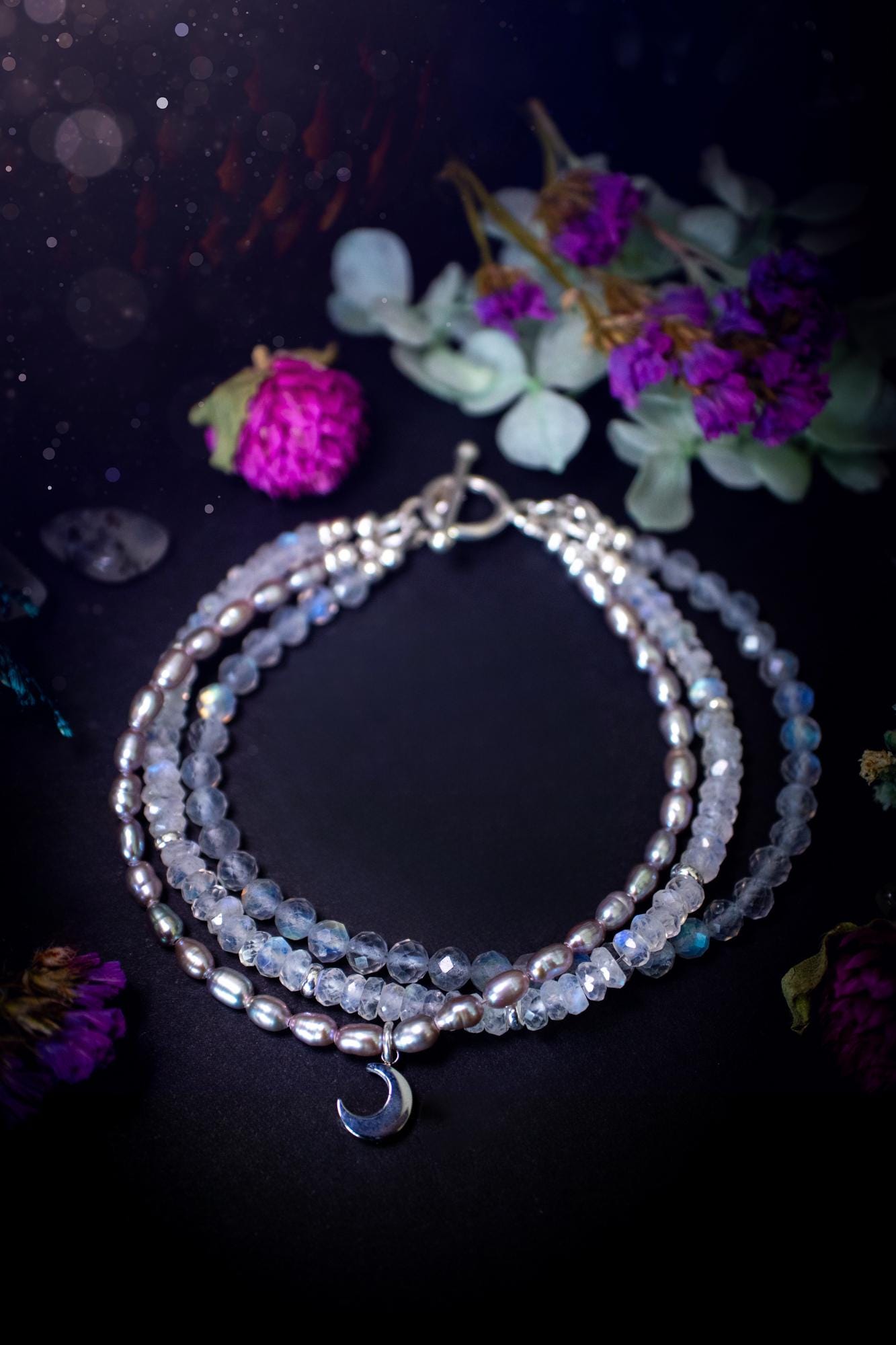 Stunning and handcrafted, triple crystal beaded bracelet. This beautiful bracelet consists of three bracelets in one all held together with a sterling silver t-bar toggle clasp. Featuring stunning flashy rainbow moonstone, light coloured labradorite, and grey to purple fresh water pearls. The findings on this bracelet are sterling silver, with a stainless steel moon charm. This piece is totally bespoke and full of celestial vibes. Ideal for any crystal and jewellery lover. Witchy and gothic