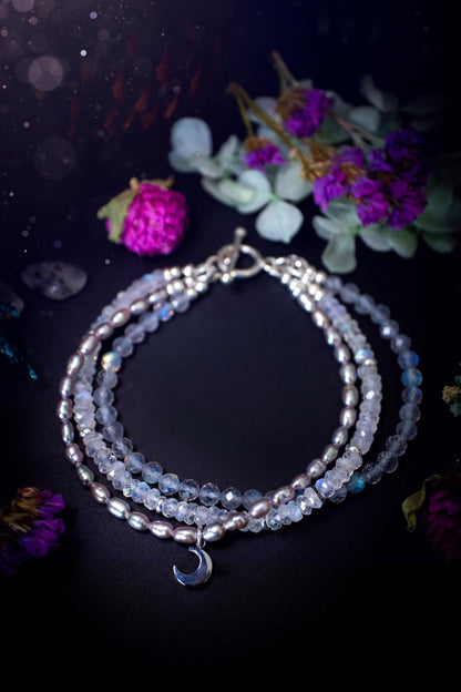 Stunning and handcrafted, triple crystal beaded bracelet. This beautiful bracelet consists of three bracelets in one all held together with a sterling silver t-bar toggle clasp. Featuring stunning flashy rainbow moonstone, light coloured labradorite, and grey to purple fresh water pearls. The findings on this bracelet are sterling silver, with a stainless steel moon charm. This piece is totally bespoke and full of celestial vibes. Ideal for any crystal and jewellery lover. Witchy and gothic