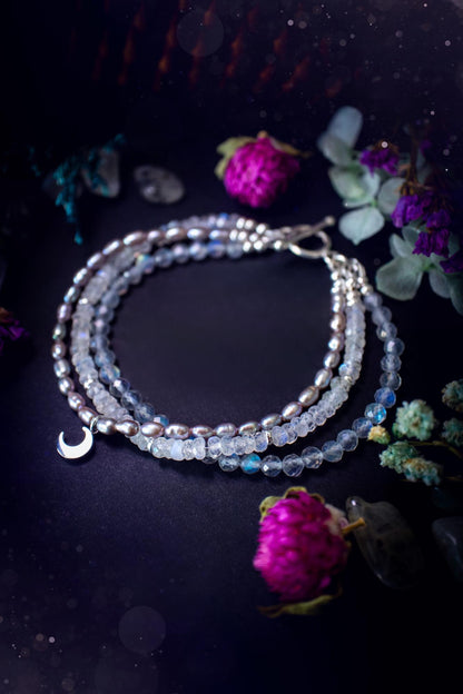 Stunning and handcrafted, triple crystal beaded bracelet. This beautiful bracelet consists of three bracelets in one all held together with a sterling silver t-bar toggle clasp. Featuring stunning flashy rainbow moonstone, light coloured labradorite, and grey to purple fresh water pearls. The findings on this bracelet are sterling silver, with a stainless steel moon charm. This piece is totally bespoke and full of celestial vibes. Ideal for any crystal and jewellery lover. Witchy and gothic